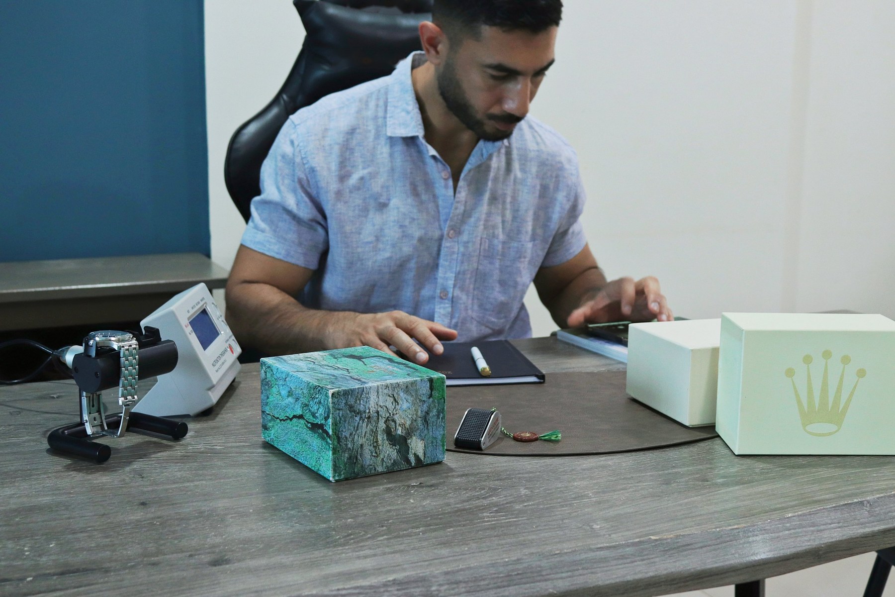 Ahmed of CrownReference at his desk, with a watch on the timegrapher and Rolex boxes
